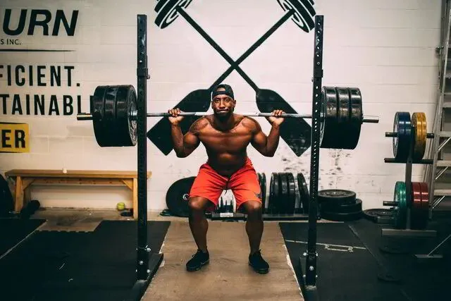Adult lifter set up under a loaded barbell in a squat rack, coached through a back squat